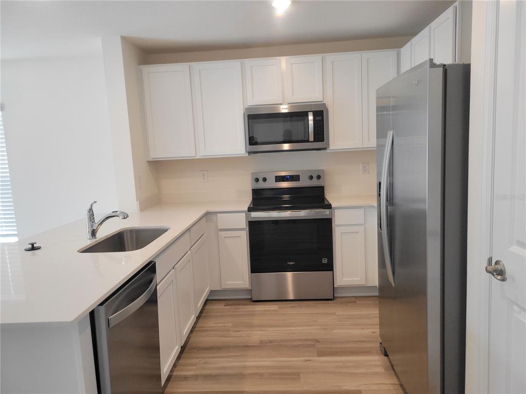 A kitchen with white cabinets, stainless steel appliances, and light-colored wood-look flooring — 6534 SW 82ND LOOP, OCALA, FL