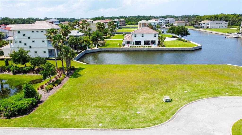 An aerial view shows a vacant grassy lot bordered by a canal and residential houses — 8 SCHOONER CIRCLE, PALM COAST, FL