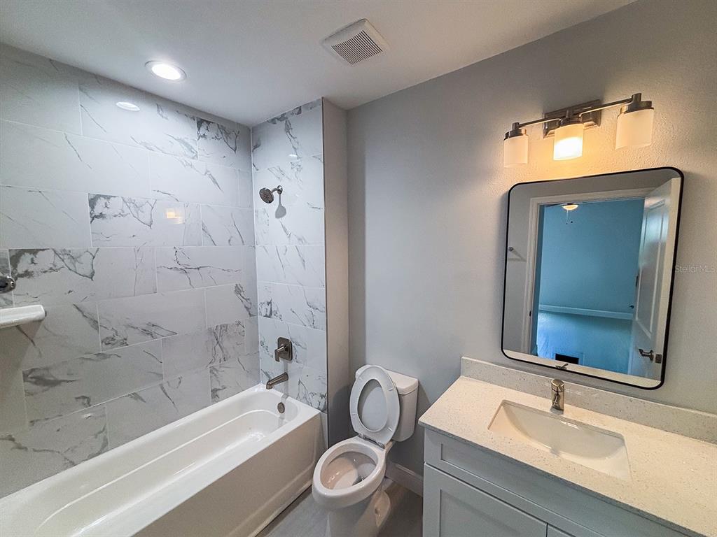 A bathroom features a marble-tiled shower-tub combo, a white vanity, and a wall-mounted mirror — 24 TROUT WAY, KISSIMMEE, FL