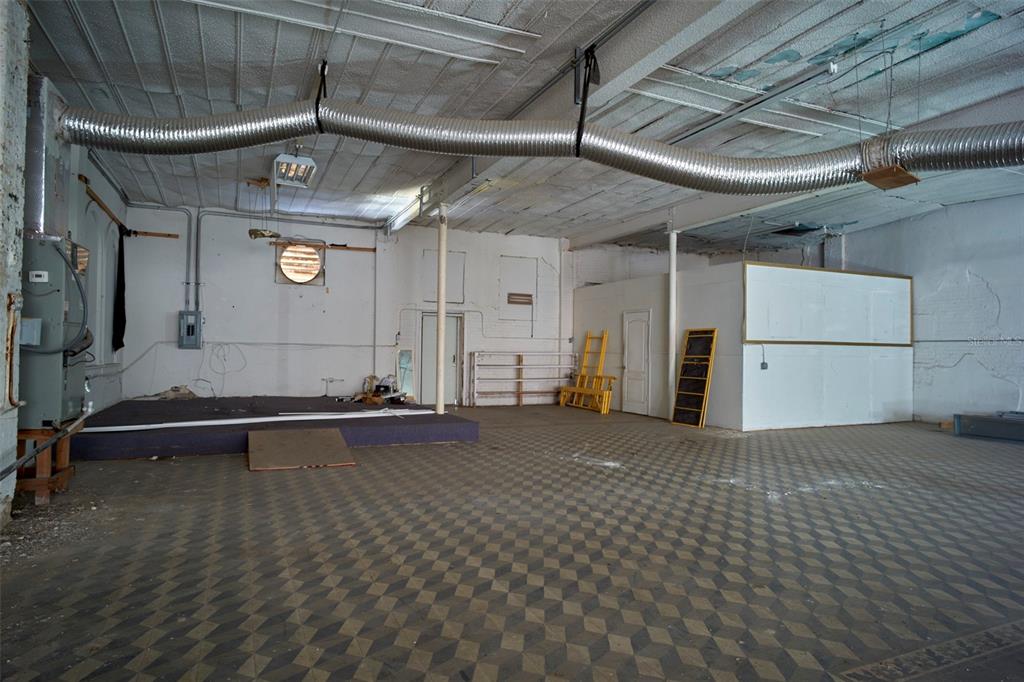 An empty commercial space features a raised stage, checkered flooring, and exposed ceiling ductwork — 2001 N HOWARD AVENUE, TAMPA, FL
