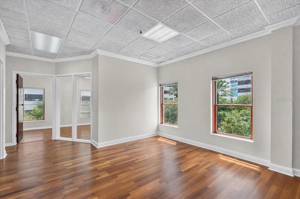An empty office room with wood flooring, a drop ceiling, and windows overlooking trees — 100 2ND AVENUE N UNIT 350, ST PETERSBURG, FL