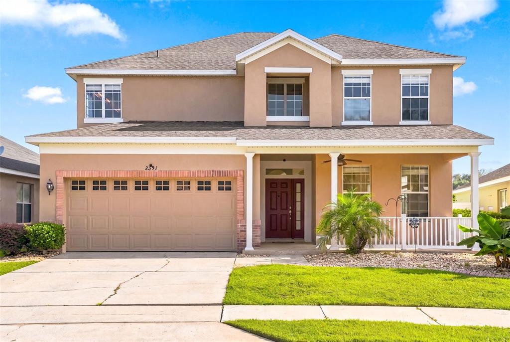 A two-story tan stucco house features a two-car garage and a front porch — 2391 SABASTIAN ST, MOUNT DORA, FL