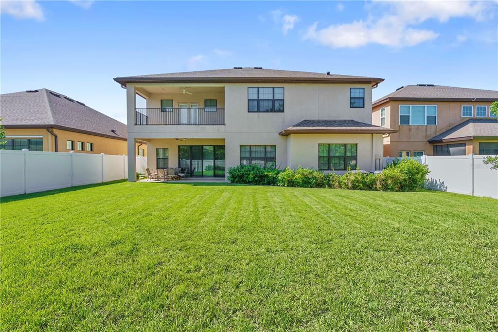The rear exterior of a two-story house features a covered balcony and a large lawn — 13830 MOONSTONE CANYON DRIVE, RIVERVIEW, FL