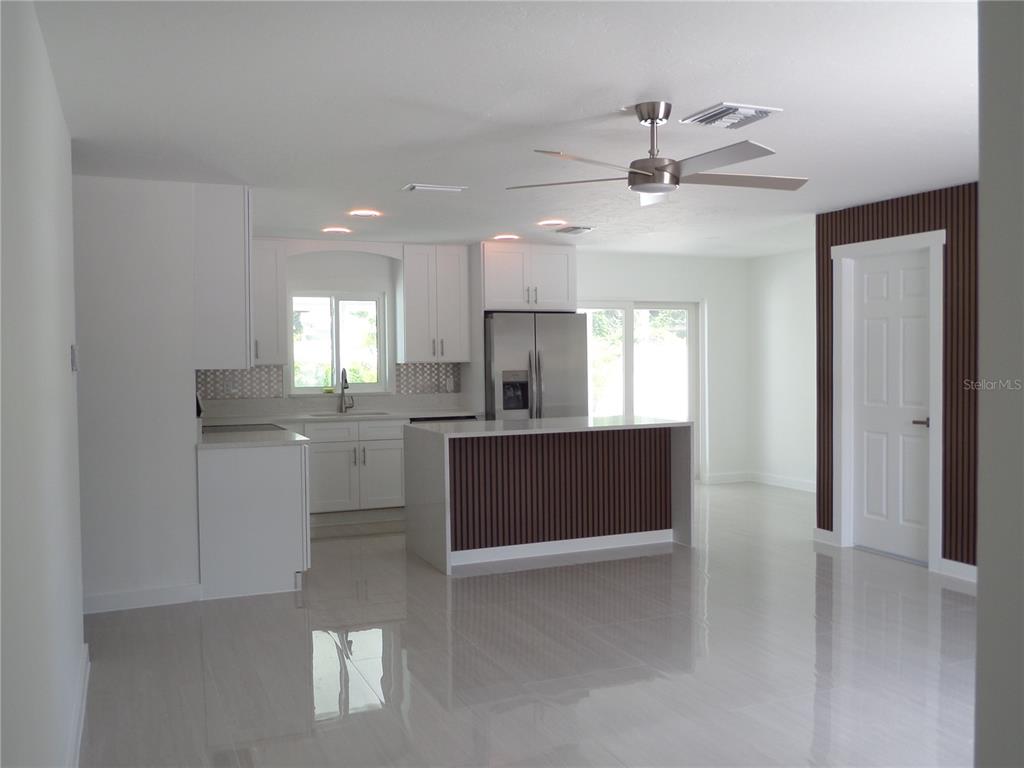 A modern kitchen features white cabinets, a slatted wood island, and light-colored tile flooring — 4925 SILK OAK DRIVE, SARASOTA, FL