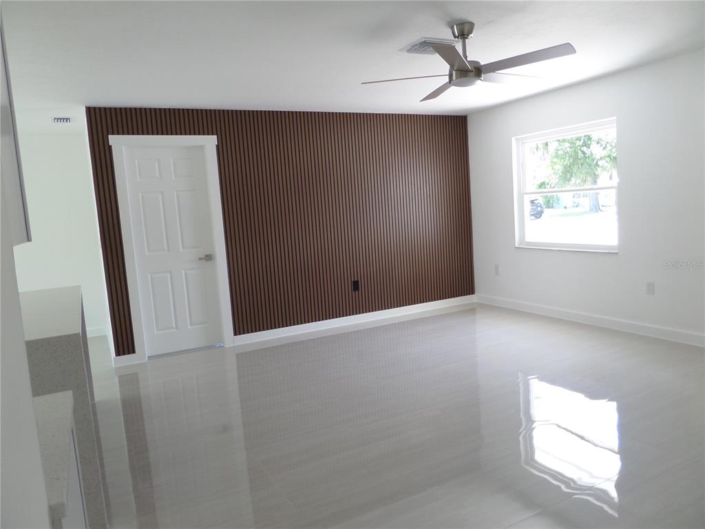 A room with light-colored tile flooring, a ceiling fan, and a dark wood-slatted accent wall — 4925 SILK OAK DRIVE, SARASOTA, FL