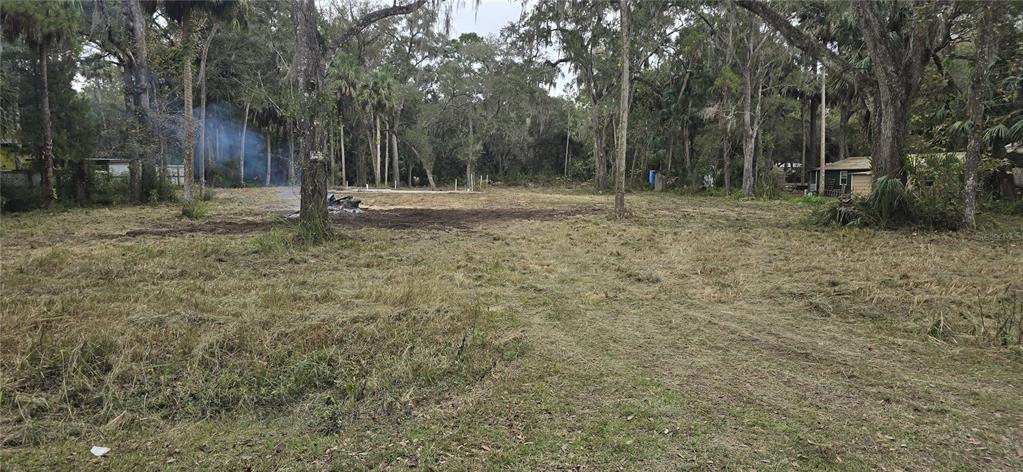 A cleared, grassy lot features scattered trees and a small area of smoldering debris — 407 SHEARER STREET, INGLIS, FL