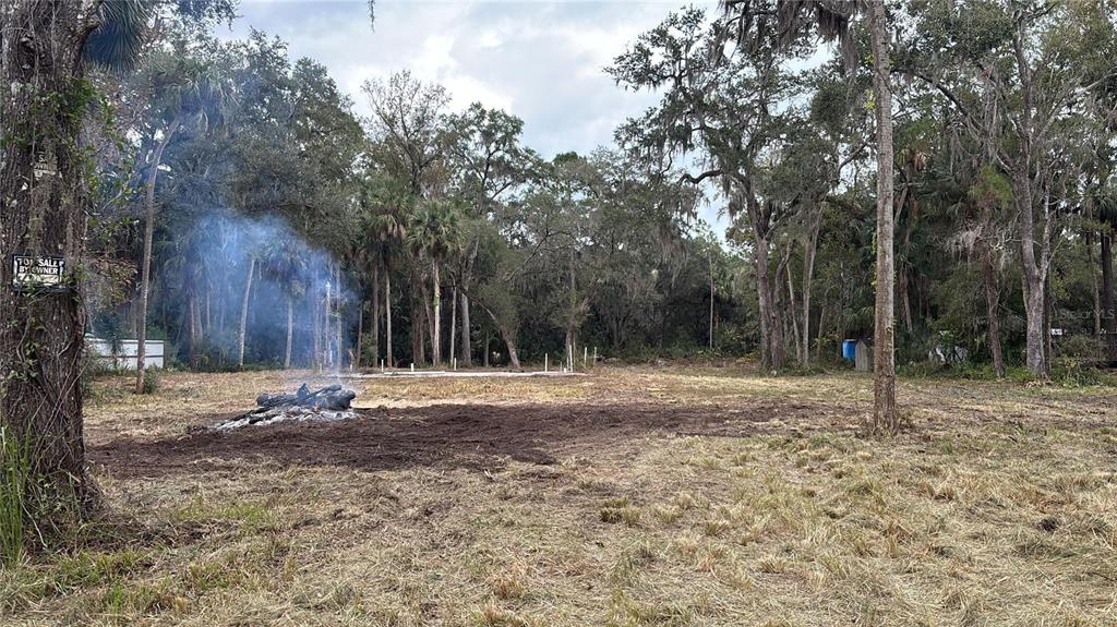 A cleared, grassy lot features a small fire with smoke and a concrete foundation slab — 407 SHEARER STREET, INGLIS, FL