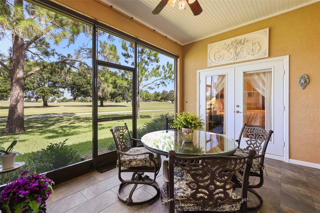 A screened-in patio with a glass-top table, metal chairs, and a view of a golf course — 29925 CYPRESS POINTE, TAVARES, FL