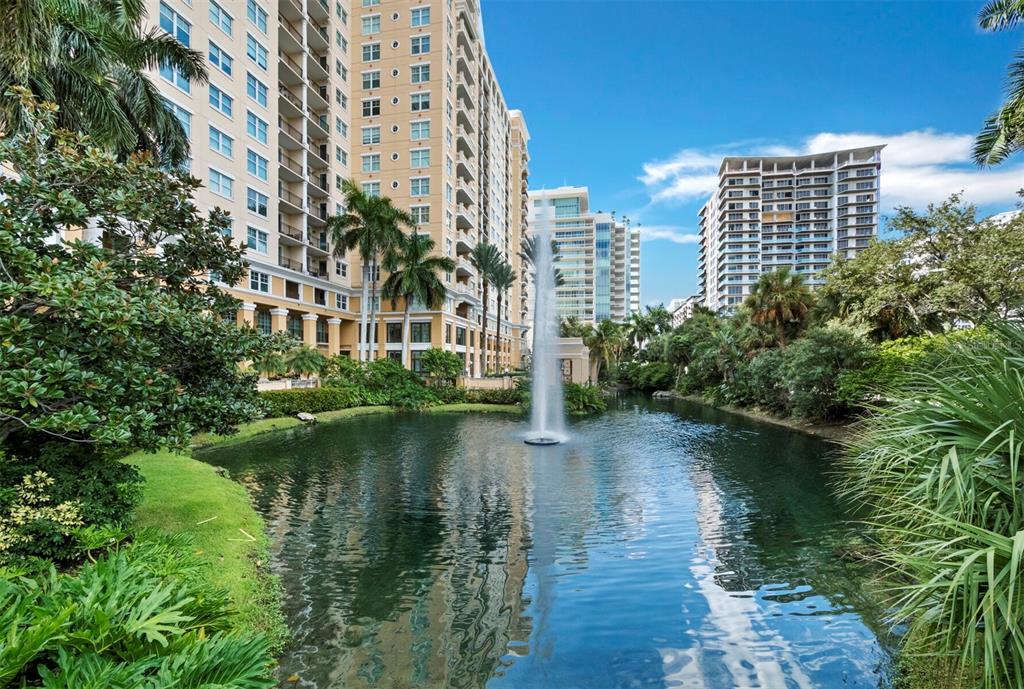 A fountain sits in a pond surrounded by lush landscaping and tall residential apartment buildings — 750 N TAMIAMI TRAIL UNIT 906, SARASOTA, FL