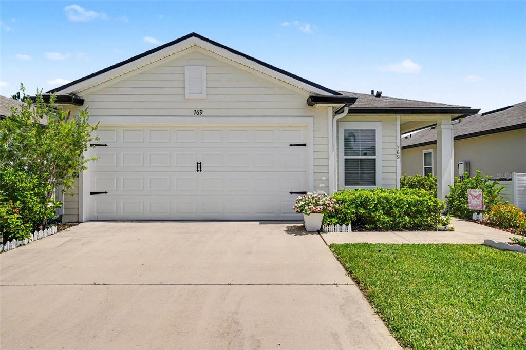A single-story house with a white garage door, light siding, and a concrete driveway — 769 GRAND RESERVE DRIVE, BUNNELL, FL