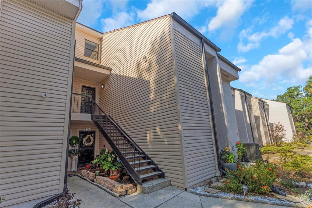 An exterior view of a two-story apartment building with beige siding and an outdoor staircase — 5151 PURITAN CIRCLE UNIT 1022, TAMPA, FL