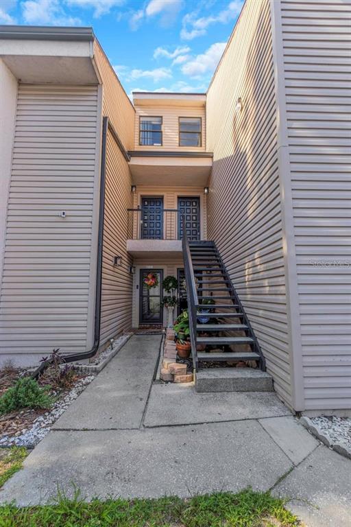 An exterior view shows a multi-story building with beige siding, a concrete walkway, and metal stairs — 5151 PURITAN CIRCLE UNIT 1022, TAMPA, FL