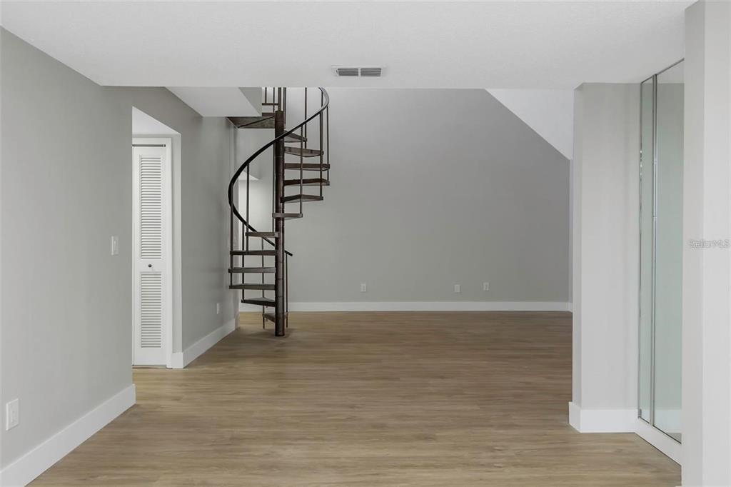 A room with light wood-look flooring, gray walls, and a dark metal spiral staircase — 5151 PURITAN CIRCLE UNIT 1022, TAMPA, FL