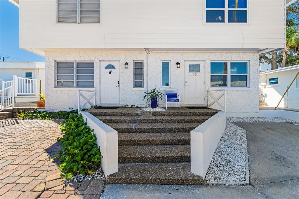 A two-story duplex with white siding and stone masonry features a brick-paved driveway — 6020 MIDNIGHT PASS ROAD UNIT 49, SARASOTA, FL