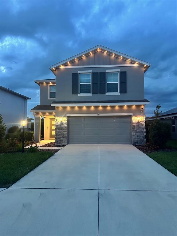 A two-story house with a gray exterior, stone accents, and a two-car garage at dusk — 17111 BARNWOOD PLACE, BRADENTON, FL