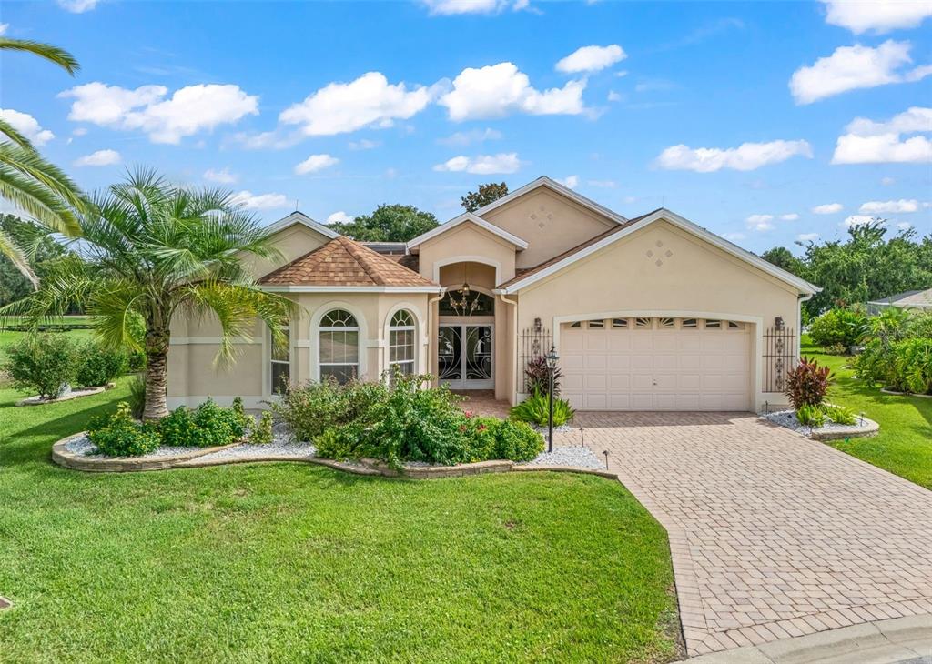 A single-story house with a beige stucco exterior, a paved driveway, and a two-car garage — 1802 ESTAFANA WAY, THE VILLAGES, FL