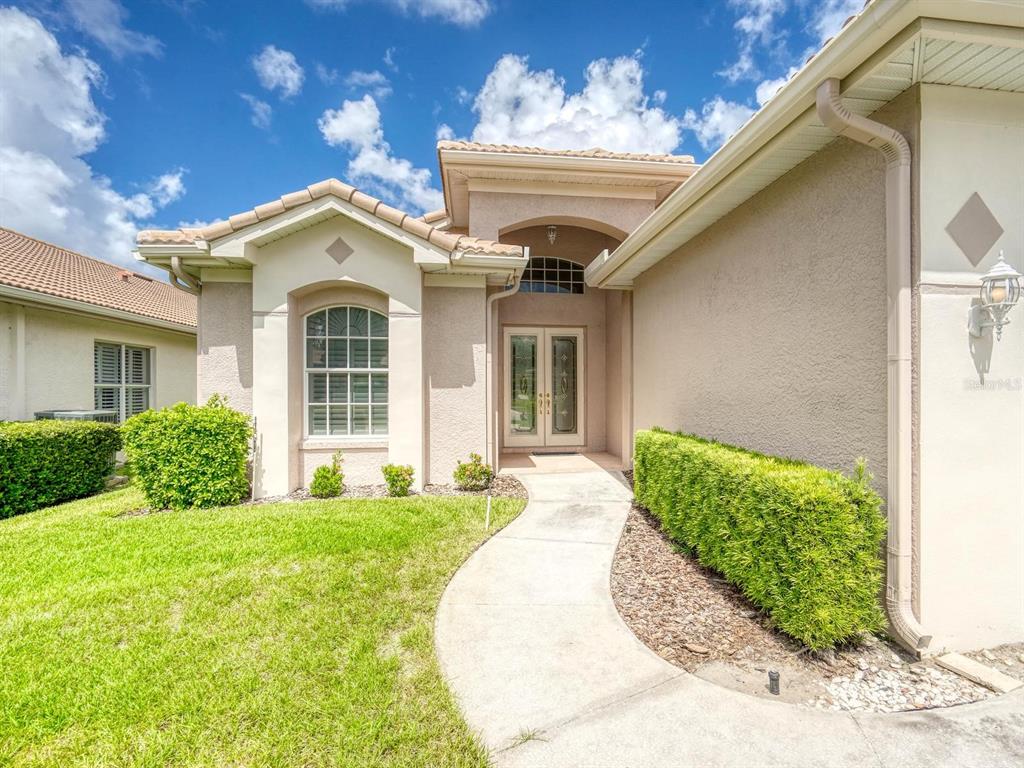 A beige stucco house exterior features a curved walkway leading to a double-door front entrance — 3944 SILK OAK LANE, PALM HARBOR, FL