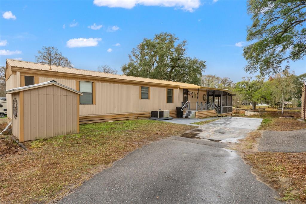A tan manufactured home with a metal roof, a shed, and a screened-in porch — 7154 CO RD 651, BUSHNELL, FL
