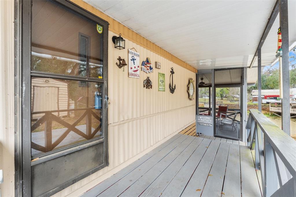 A covered wooden porch with a screen door and nautical wall decor overlooks a yard — 7154 CO RD 651, BUSHNELL, FL