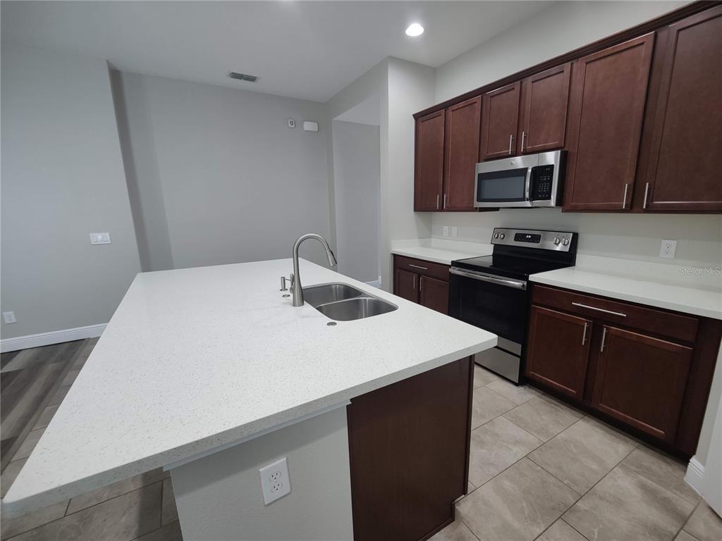 A kitchen features a white quartz island, dark wood cabinets, and stainless steel appliances — 9042 YONATH STREET, ORLANDO, FL