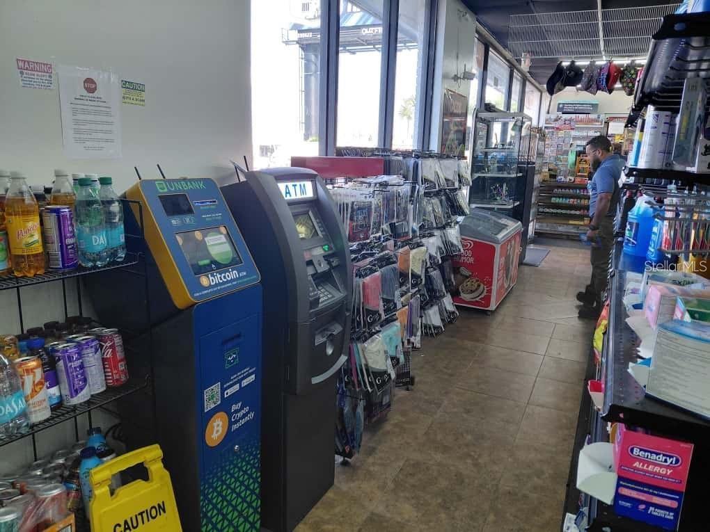 A convenience store interior features a Bitcoin ATM, a standard ATM, and various retail merchandise shelves — 7906 W HILLSBOROUGH AVENUE, TAMPA, FL
