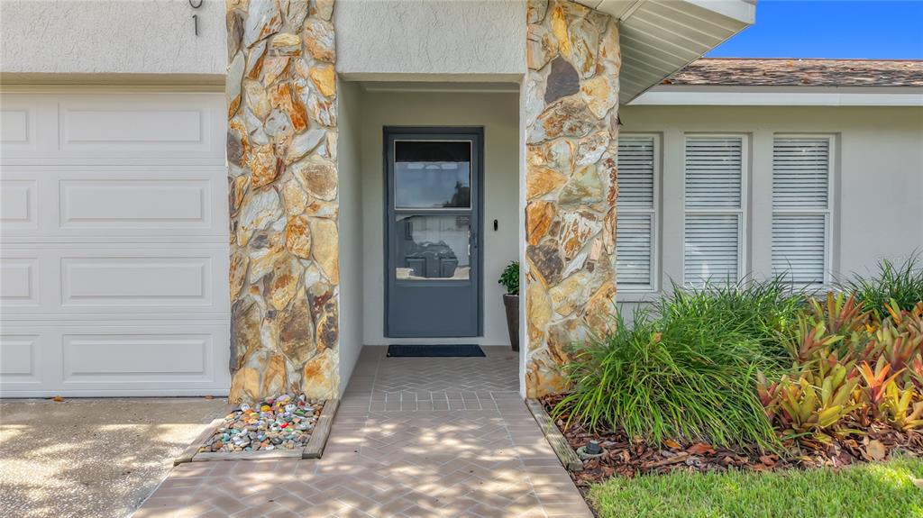 A stone-accented entryway leads to a gray front door with a herringbone-patterned walkway — 13101 116TH STREET, LARGO, FL