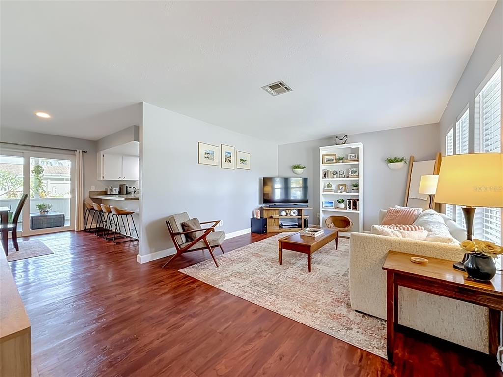 A living room with wood-look flooring, a white bookshelf, a television, and an adjacent kitchen — 13101 116TH STREET, LARGO, FL