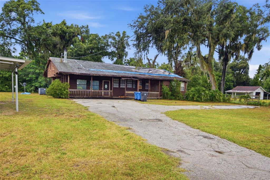 A brown wooden house with a blue tarp on the roof sits on a grassy lot — 1810 BLAND WAY, DOVER, FL