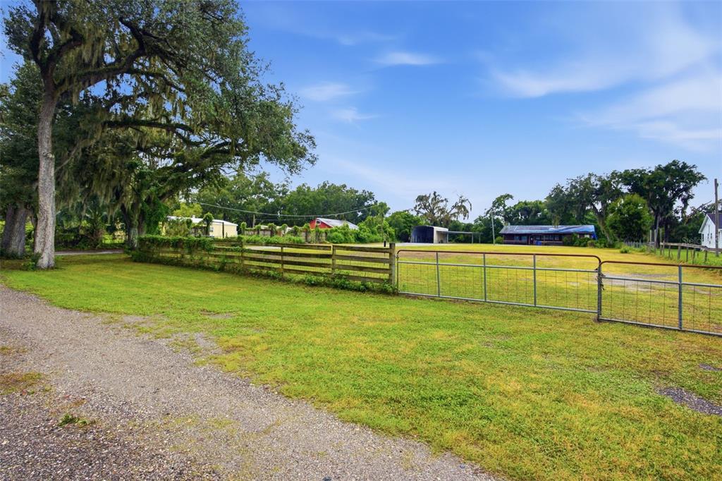 A gravel driveway leads to a fenced grassy field with trees and several distant buildings — 1810 BLAND WAY, DOVER, FL