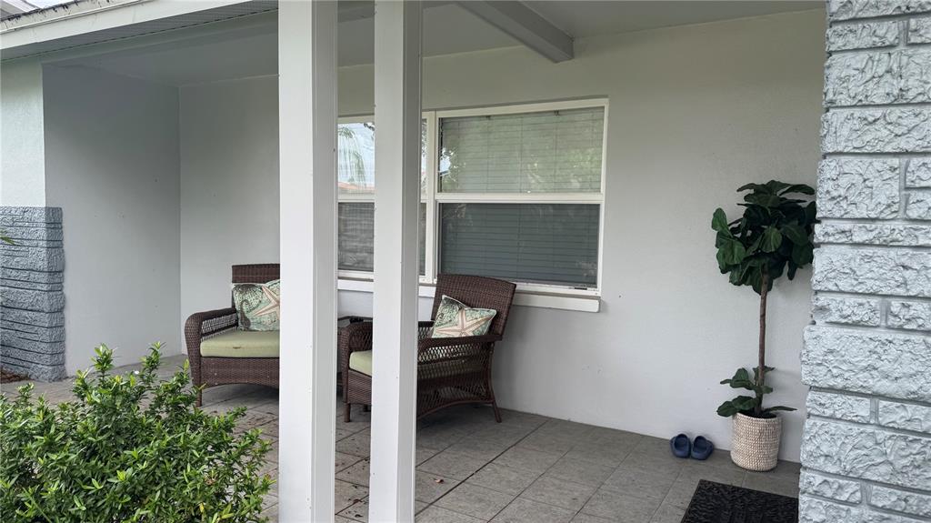 A covered patio features tiled flooring, two wicker chairs, and a potted artificial plant — 9652 COMMODORE DRIVE, SEMINOLE, FL
