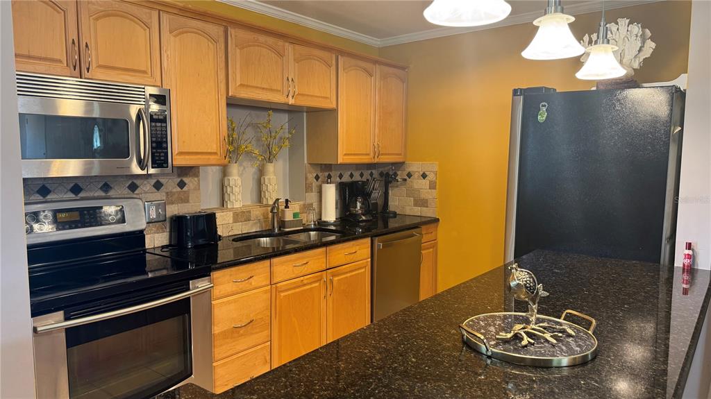 A kitchen features light wood cabinets, black granite countertops, stainless steel appliances, and yellow walls — 9652 COMMODORE DRIVE, SEMINOLE, FL