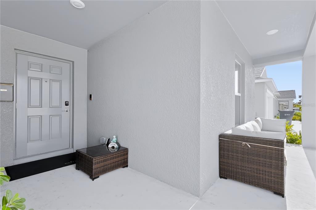A covered porch features a light gray front door, a wicker side table, and seating — 13421 NEW JADE AVENUE, WIMAUMA, FL