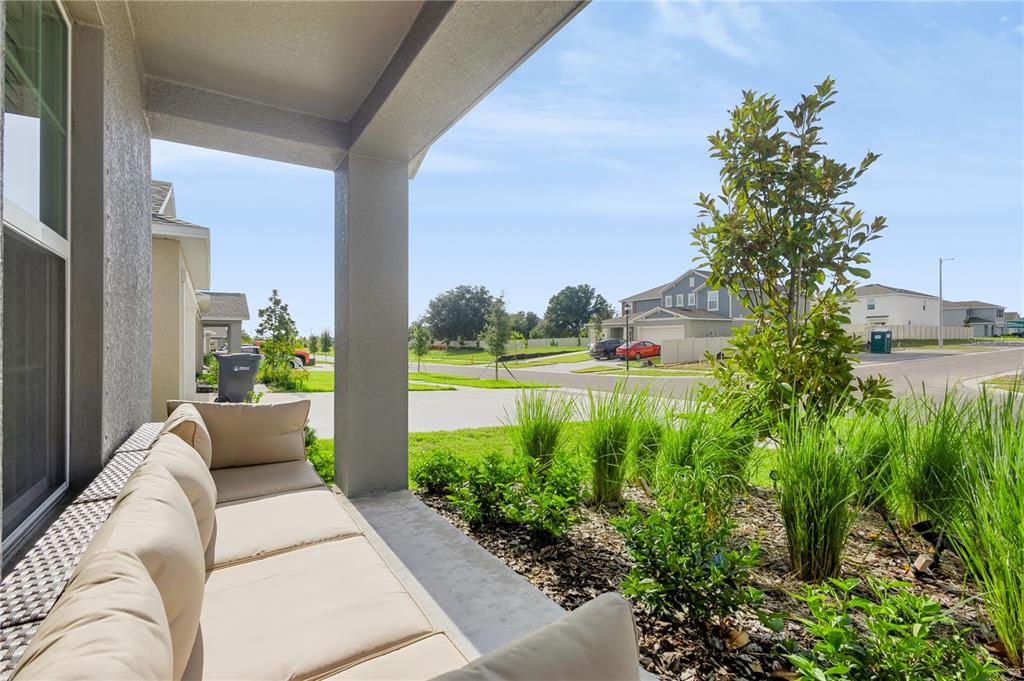 A covered porch features a beige sofa and a view of a suburban street — 13421 NEW JADE AVENUE, WIMAUMA, FL