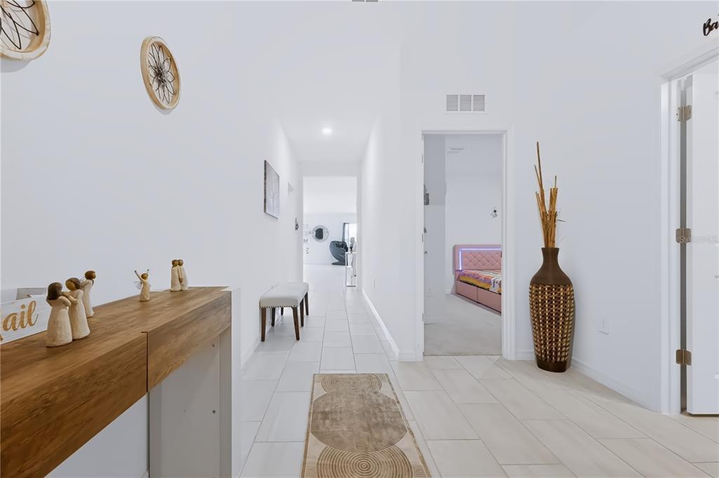 A bright hallway with white walls, tiled floors, a wooden console table, and a bedroom doorway — 13421 NEW JADE AVENUE, WIMAUMA, FL