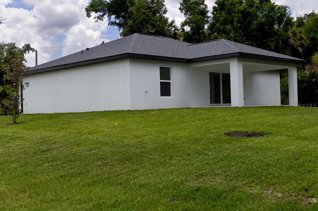 The exterior rear view of a white house with a covered patio and grassy yard — 4696 APRIL AVENUE, NORTH PORT, FL
