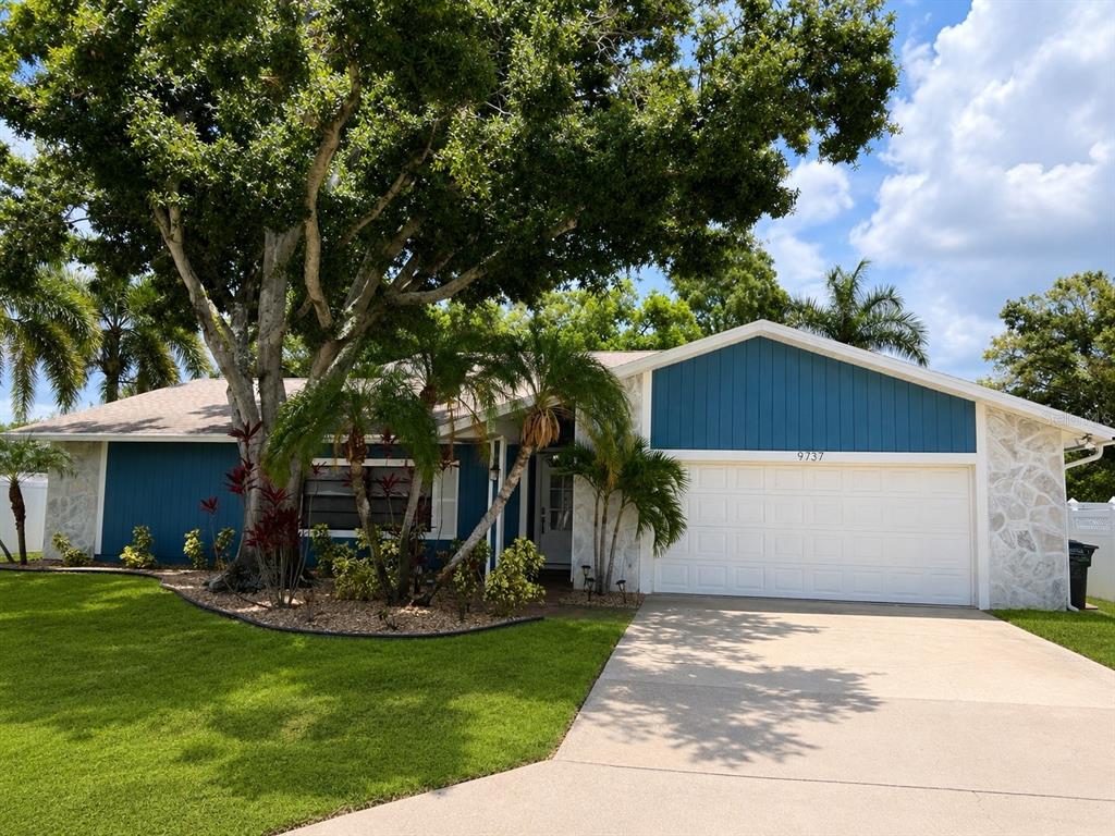 A single-story house with blue vertical siding, stone accents, a white garage door, and landscaping — 9737 135TH STREET, SEMINOLE, FL