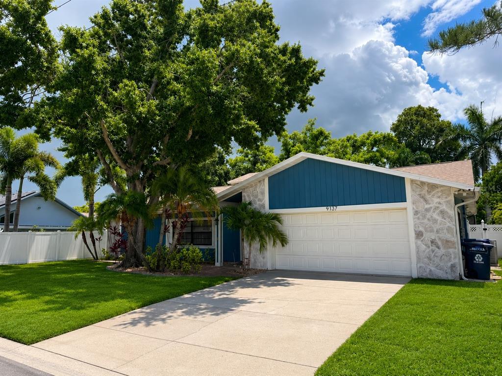 A single-story house with blue siding, stone accents, a two-car garage, and a large tree — 9737 135TH STREET, SEMINOLE, FL