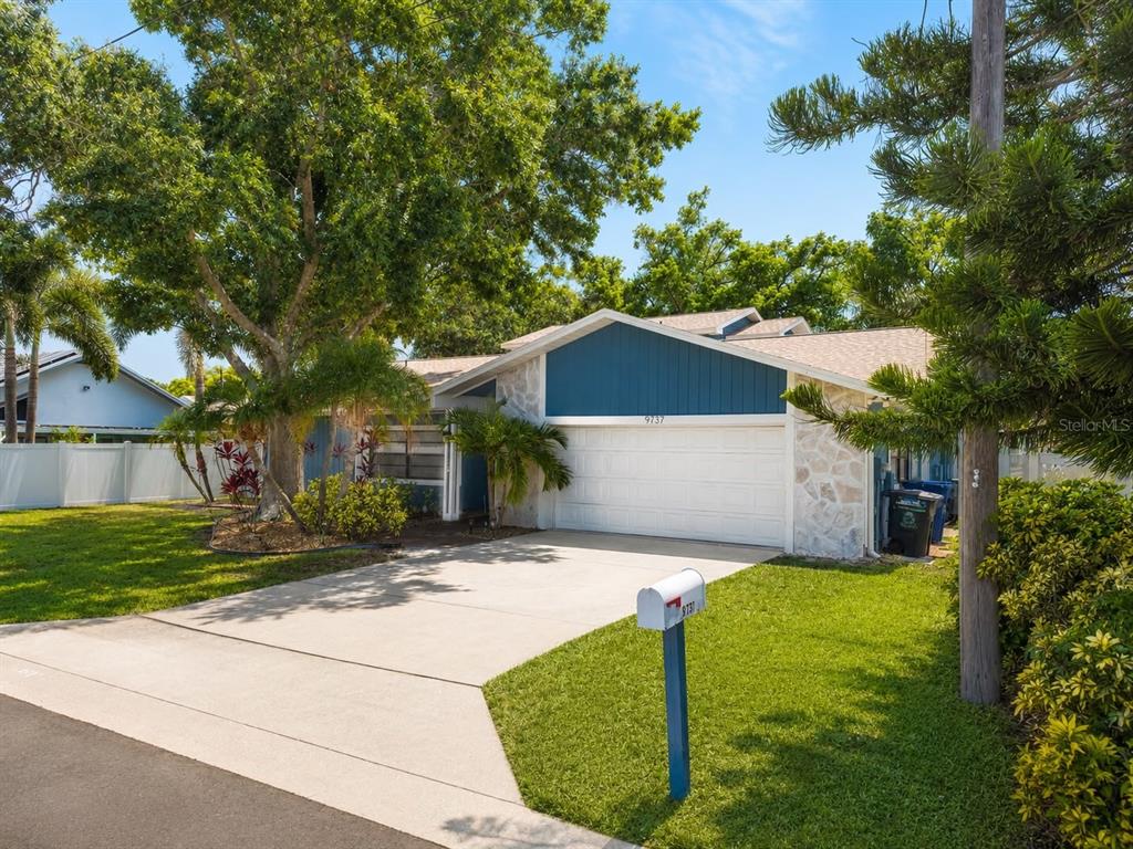 A single-story house with a white garage door, stone siding, and blue accents — 9737 135TH STREET, SEMINOLE, FL