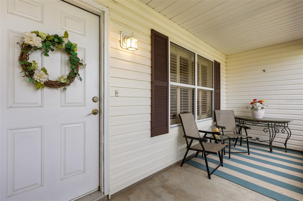 A covered front porch features a white door with a wreath, chairs, and striped rug — 2527 BOTELLO AVENUE, THE VILLAGES, FL