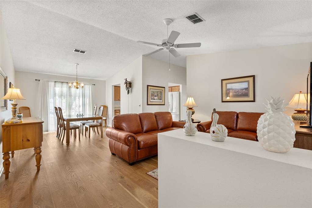 A living and dining area with wood floors, leather sofas, and a white half-wall — 2527 BOTELLO AVENUE, THE VILLAGES, FL