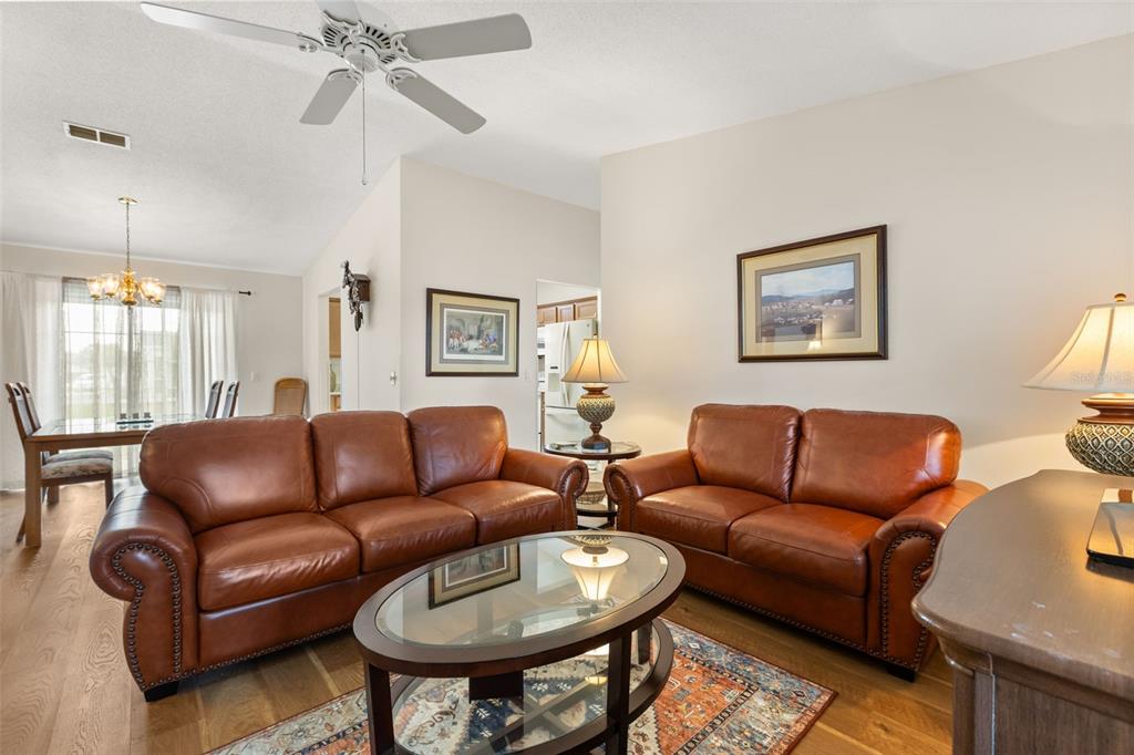 A living room features two brown leather sofas, a glass coffee table, and wood flooring — 2527 BOTELLO AVENUE, THE VILLAGES, FL