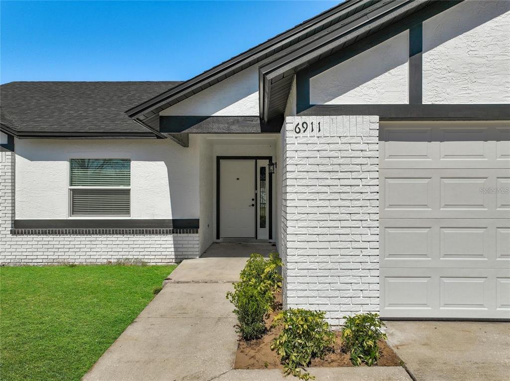 A white house exterior features a brick facade, a front door, and a garage door — 6911 CRESCENT RIDGE ROAD, ORLANDO, FL