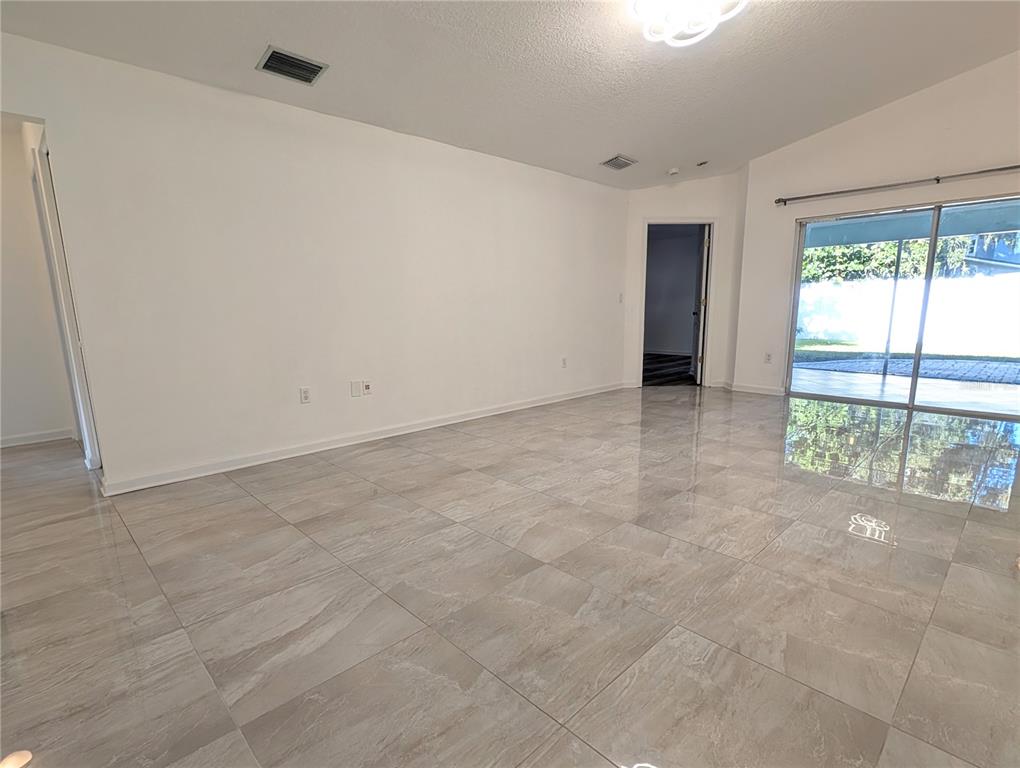 An empty living room features large light-colored tile flooring, white walls, and sliding glass doors — 4557 WORCESTER ROAD, SARASOTA, FL