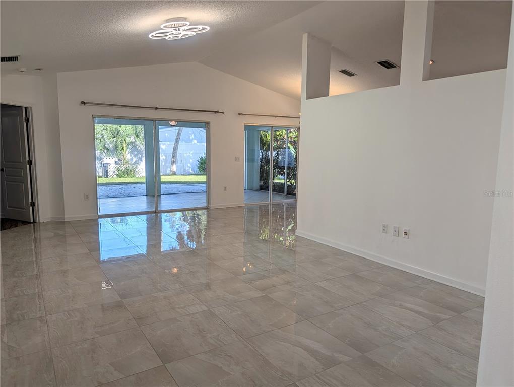 A bright living room features large sliding glass doors, light-colored tile flooring, and vaulted ceilings — 4557 WORCESTER ROAD, SARASOTA, FL