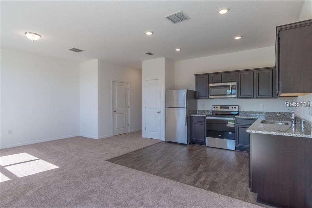 An open-concept kitchen with dark cabinets and stainless steel appliances sits beside a carpeted living area — 342 MADISON DRIVE, DAVENPORT, FL