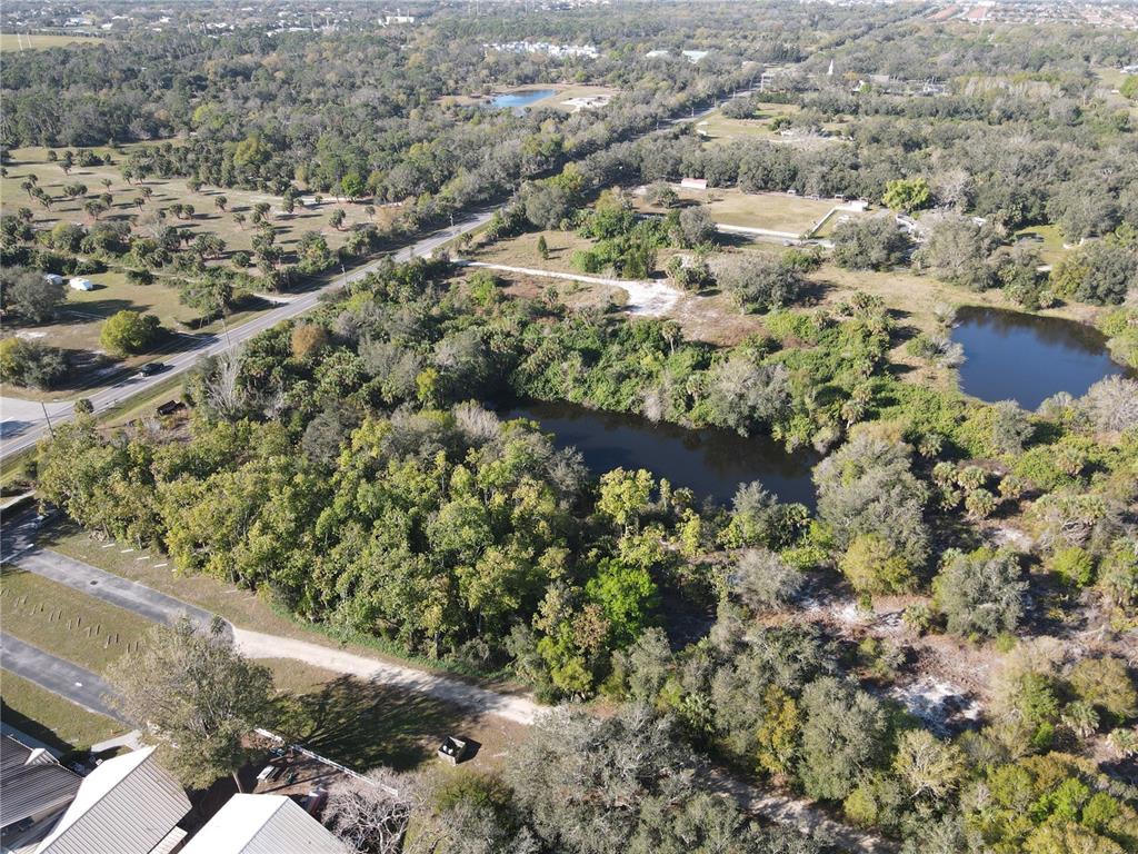 An aerial view shows a wooded lot with a pond and a nearby road — E VENICE AVENUE, VENICE, FL