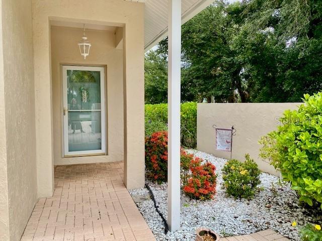 A covered entryway features a brick-paver floor, a glass storm door, and a landscaped rock garden — 1275 BERKSHIRE CIRCLE, VENICE, FL