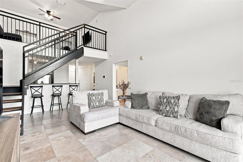 A living room features a light gray sofa, an armchair, tile flooring, and a staircase — 4221 W SPRUCE STREET UNIT 2425, TAMPA, FL