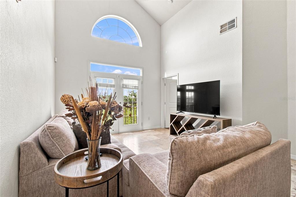 A living room features high ceilings, a large arched window, tile flooring, and a television — 4221 W SPRUCE STREET UNIT 2425, TAMPA, FL