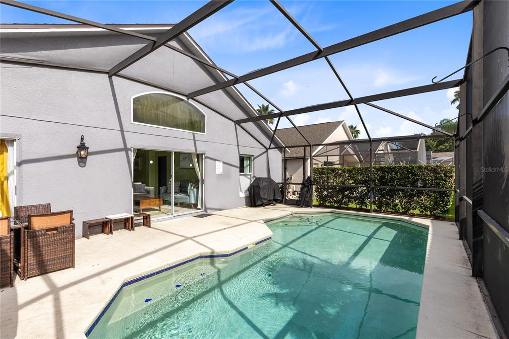 A screened-in patio features a swimming pool, concrete deck, and a view of the house — 915 LAKE BERKLEY DRIVE, KISSIMMEE, FL